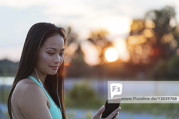 Frau benutzt Smartphone beim Musikhören während des Sonnenuntergangs