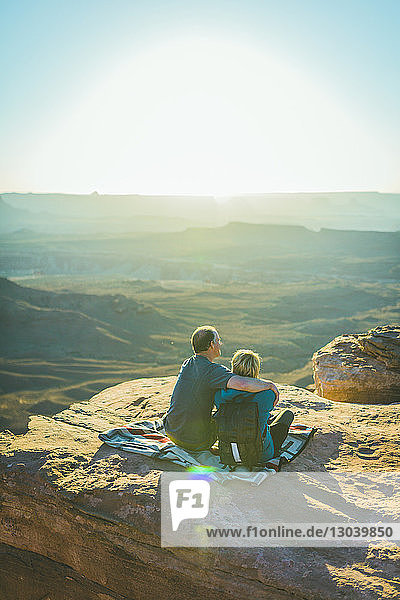 Rückansicht eines Paares  das an einem sonnigen Tag im Canyonlands-Nationalpark auf einem Berg sitzt