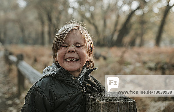 Playful boy with eyes closed clenching teeth by wooden fence at Yosemite National Park
