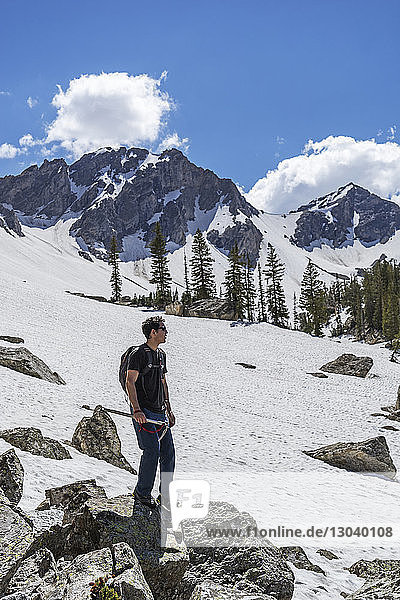 Full length of man standing on rocks at snowcapped mountain against sky