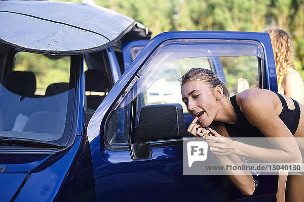 Frau trägt Lippenbalsam auf  während sie in den Seitenspiegel eines Autos schaut