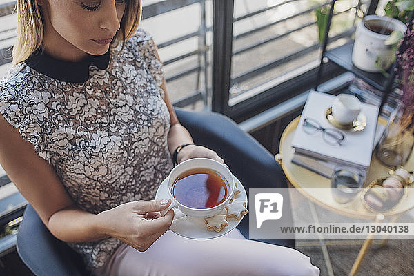 Schrägansicht einer Geschäftsfrau  die eine Kaffeetasse hält  während sie im Heimbüro auf einem Stuhl sitzt