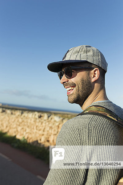 Seitenansicht eines lächelnden Wanderers mit Sonnenbrille vor strahlend blauem Himmel