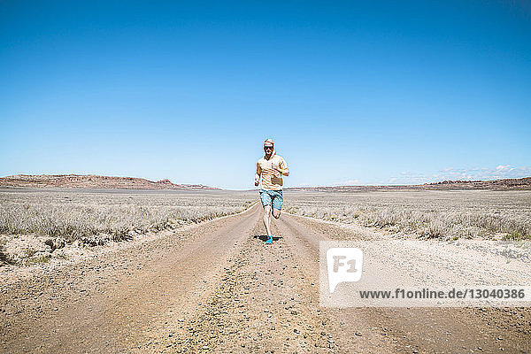 Mann läuft in voller Länge auf unbefestigter Straße vor blauem Himmel