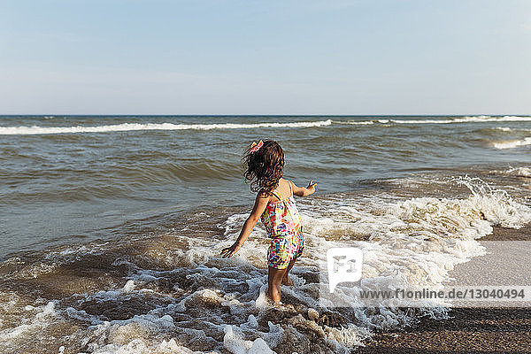 Unbeschwertes Mädchen spielt in Wellen am Strand vor klarem Himmel