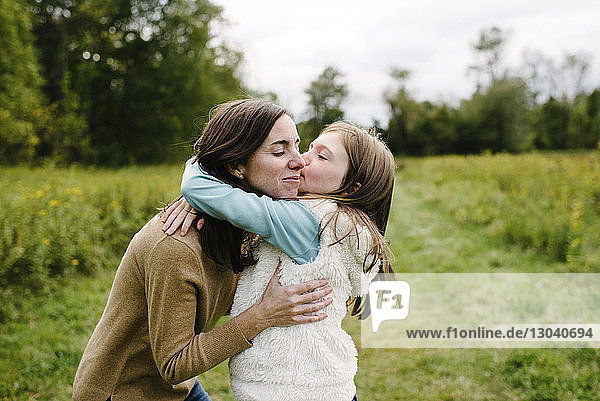 Daughter kissing mother while standing at park during winter