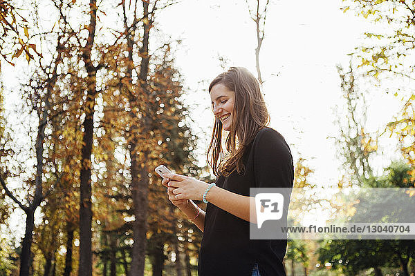 Niedriger Blickwinkel einer Frau  die ein Smartphone benutzt  während sie an Bäumen steht
