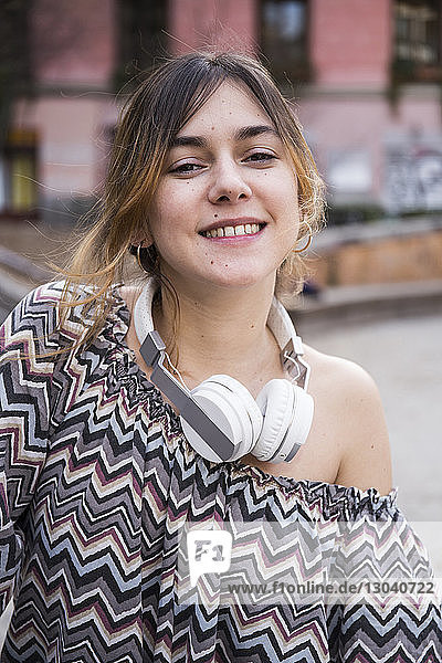 Porträt einer lächelnden Frau mit Kopfhörern  die in der Stadt steht