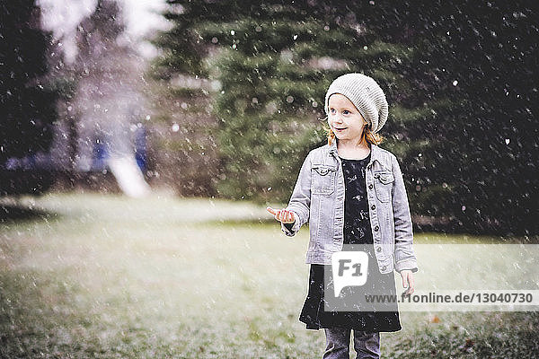 Lächelndes Mädchen steht bei Schneefall auf Grasfeld im Park