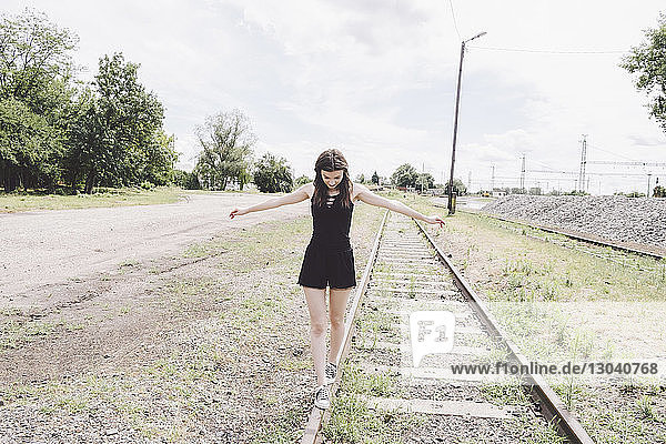 Full length of young woman with arms outstretched walking on railroad track
