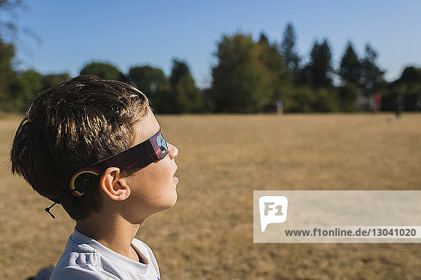 Side view of boy wearing 3-D glasses while looking away at field during sunny day