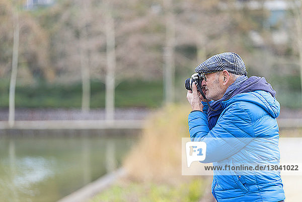 Side view of man photographing with camera at park