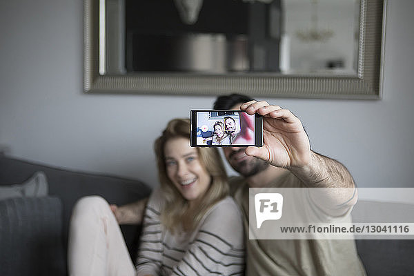 Mann nimmt Selfie mit Freundin  während er zu Hause auf dem Sofa sitzt