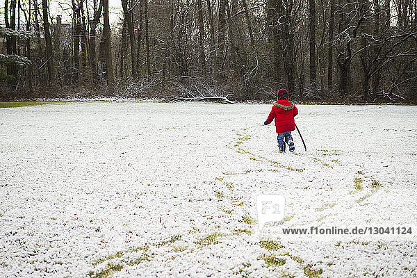 Rear view of boy holding stick while walking on snowy field
