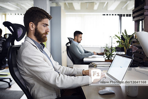 Side view of businessman using laptop in creative office