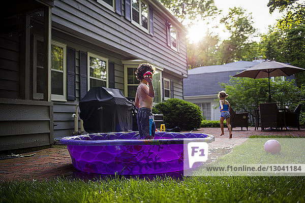 Girl running while brother standing in wading pool at backyard