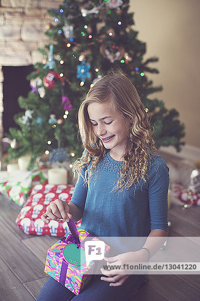 Mädchen hält Weihnachtsgeschenk  während sie zu Hause auf dem Boden sitzt
