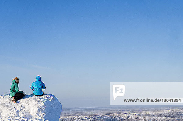 Friends sitting on mountain against clear sky