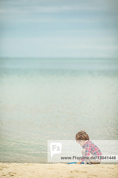 Seitenansicht eines Jungen  der am Strand mit Sand spielt