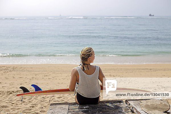 Rear view of woman with surfboard sitting at beach