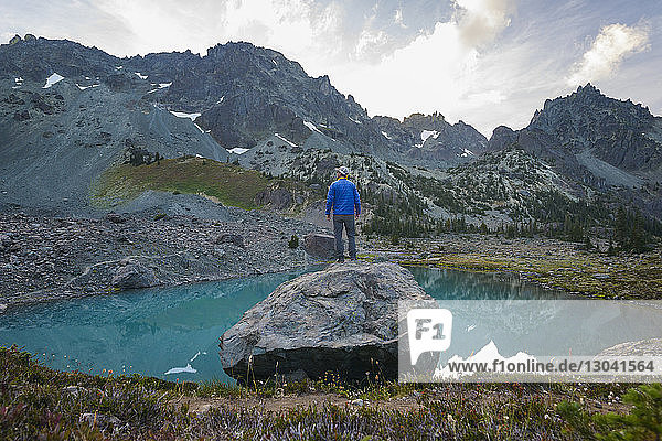 Rear view of hiker standing on rock by lake against mountains at Olympic National Park
