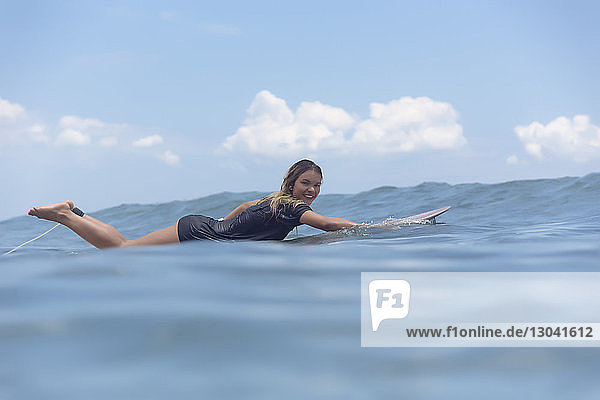 Full length portrait of carefree smiling woman lying on surfboard while swimming in sea