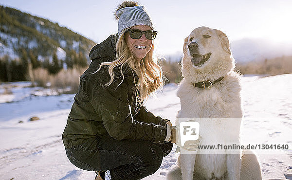 Glückliche Frau mit Sonnenbrille und Hund auf verschneitem Feld