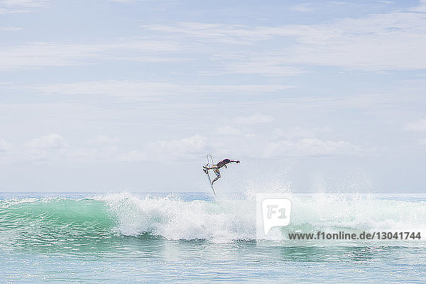 Entschlossener männlicher Surfer springt auf riesigen Meereswellen gegen den Himmel
