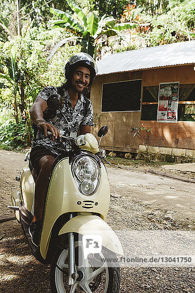 Portrait of cheerful man wearing helmet while driving motor scooter on dirt road