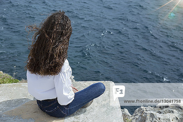 Hochwinkelaufnahme einer Frau  die auf einer Stützmauer am Meer sitzt
