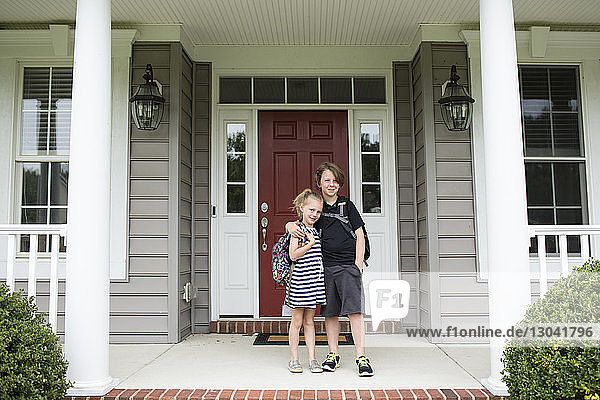Portrait of siblings with backpack standing on porch