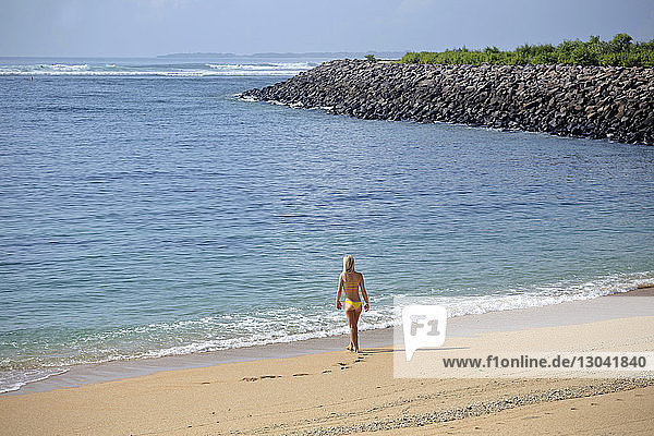 Rückansicht einer Frau im Bikini  die am Strand gegen den Himmel läuft