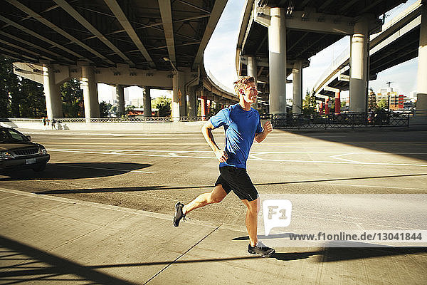Sporty man jogging on city street under bridges