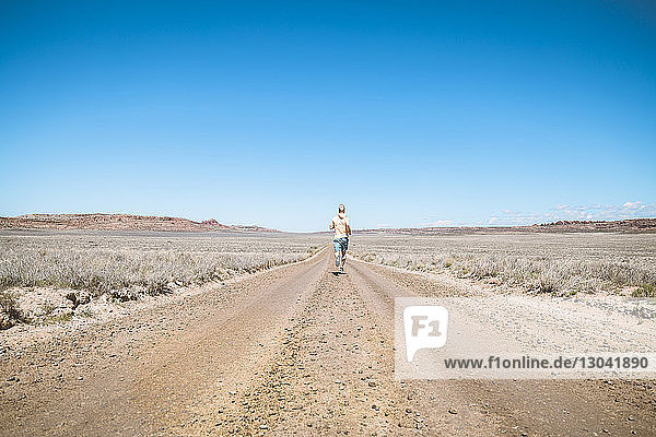 Rear view of man running on dirt road against clear blue sky