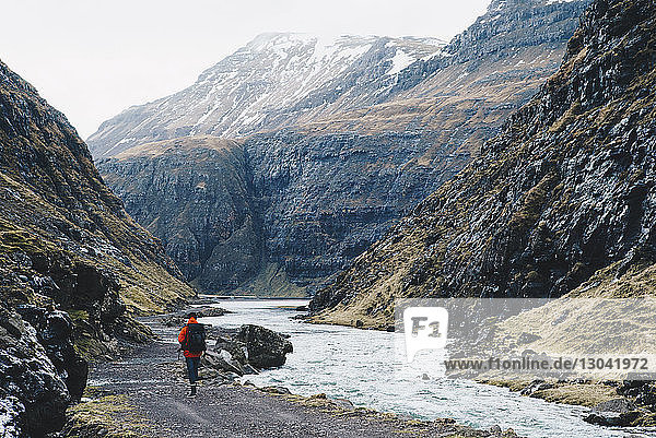 Rear view of man walking road by river against mountains
