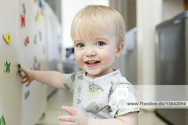 Porträt eines süßen  lächelnden Jungen  der zu Hause mit bunten Magnetbuchstaben auf einem Metallschrank spielt