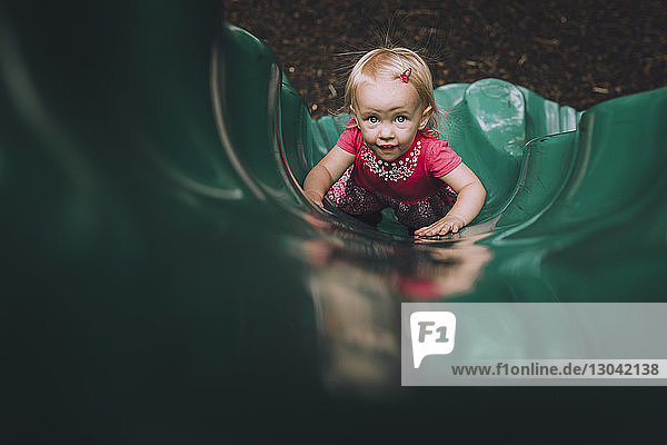 Hochwinkelporträt eines kleinen Mädchens  das auf einer Rutsche auf einem Spielplatz spielt