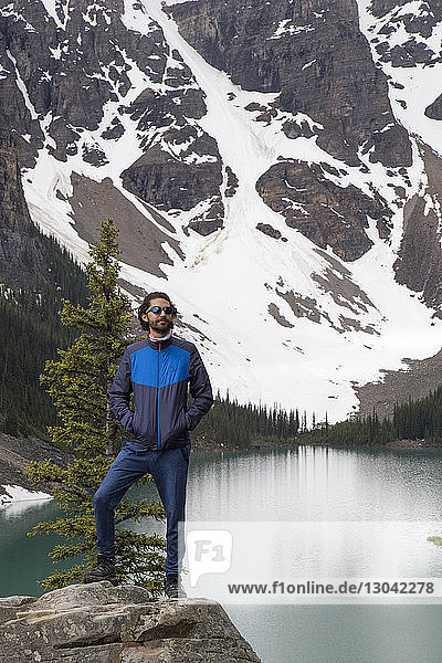 Hiker with hands in pockets standing on rock against Moraine Lake and mountain