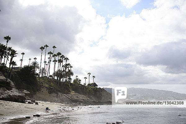 Fernansicht eines Jungen  der am Laguna Beach gegen bewölkten Himmel spielt