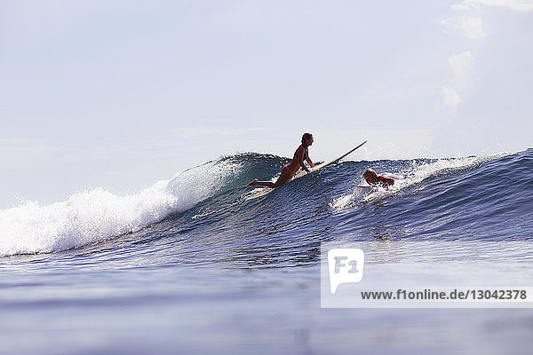 Freunde surfen auf einer Welle im Meer gegen den Himmel