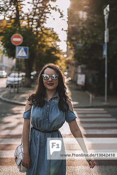 Junge Frau mit Sonnenbrille beim Überqueren der Straße in der Stadt