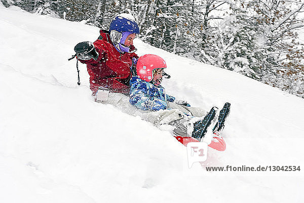 Mother with daughter tobogganing on snow covered field in forest