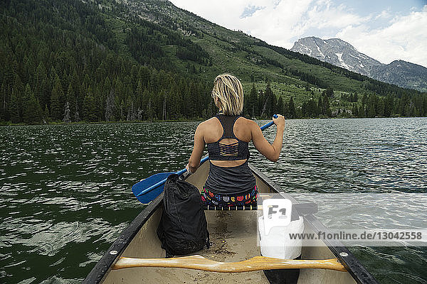 Rear view of woman rowing boat in river against mountains