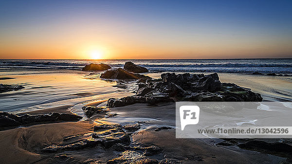 Szenische Ansicht des Meeres mit Felsen am Strand vor dramatischem Himmel bei Sonnenuntergang