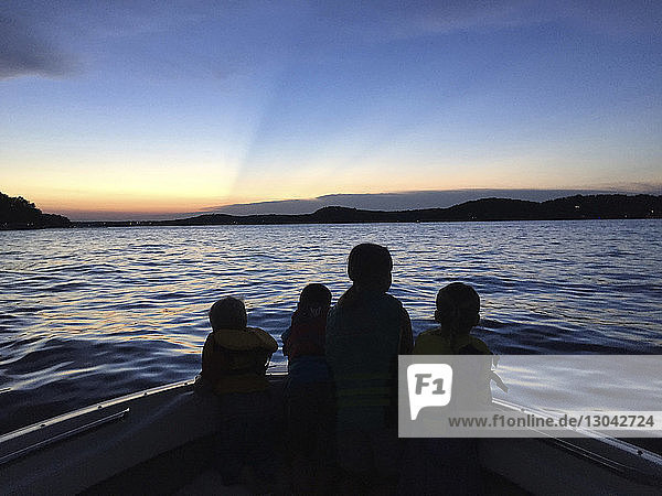 Silhouette siblings traveling in boat on Kentucky lake against blue sky during sunset