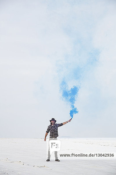 Portrait of man holding smoke bomb while standing on Bonneville Salt Flats against sky