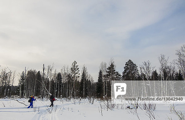 Male friends hiking on snow covered field against cloudy sky