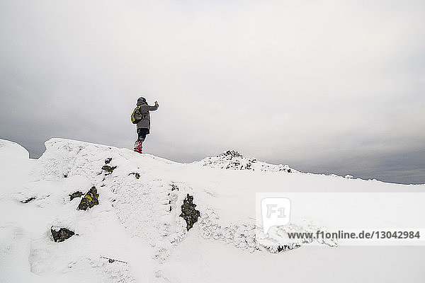 Tiefwinkelansicht eines Wanderers  der auf einem schneebedeckten Feld vor bewölktem Himmel steht