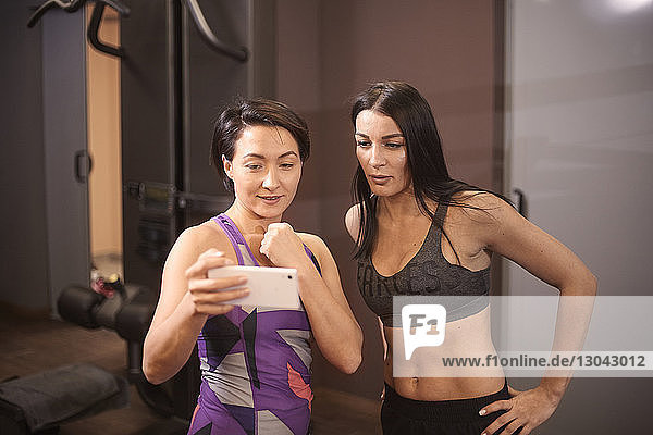 Frau zeigt einem Freund im Fitnessstudio ein Smartphone