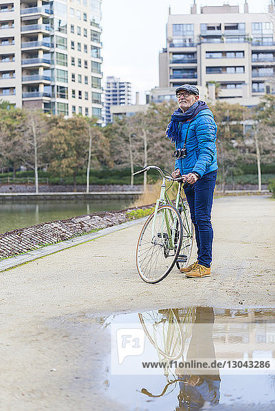 Side view of man with bicycle standing on footpath at park